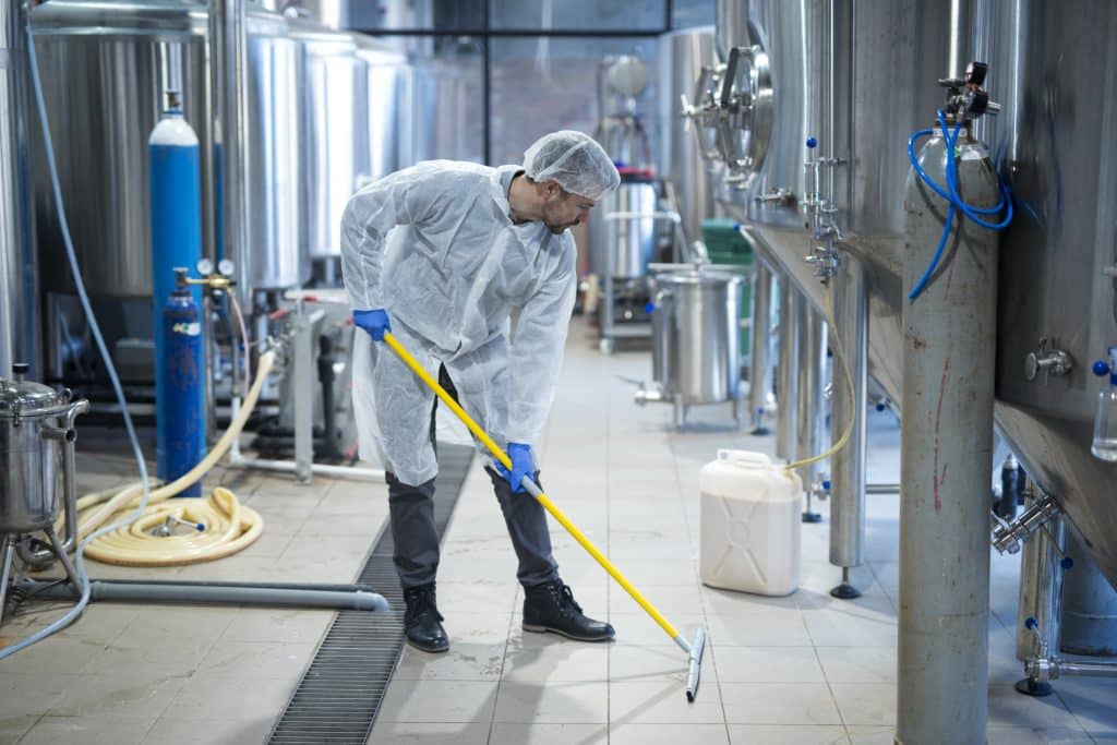 professional industrial cleaner in protective uniform cleaning floor of food processing plant scaled